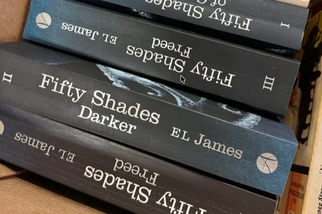 A stack of Fifty Shades of Grey trilogy paperbacks on a bookshelf