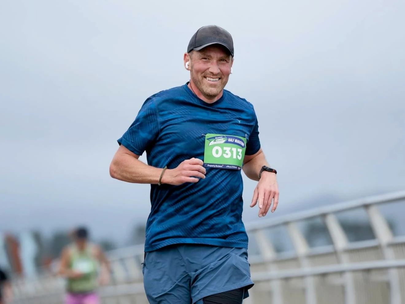 Trent smiling mid-stride during a half marathon on a bridge