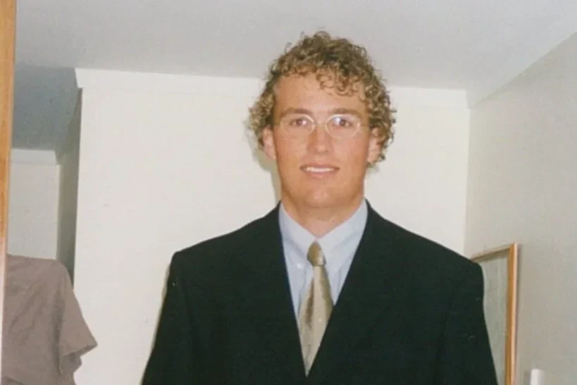 A young Trent in a suit and tie, curly-haired and bespectacled, on his first day of work
