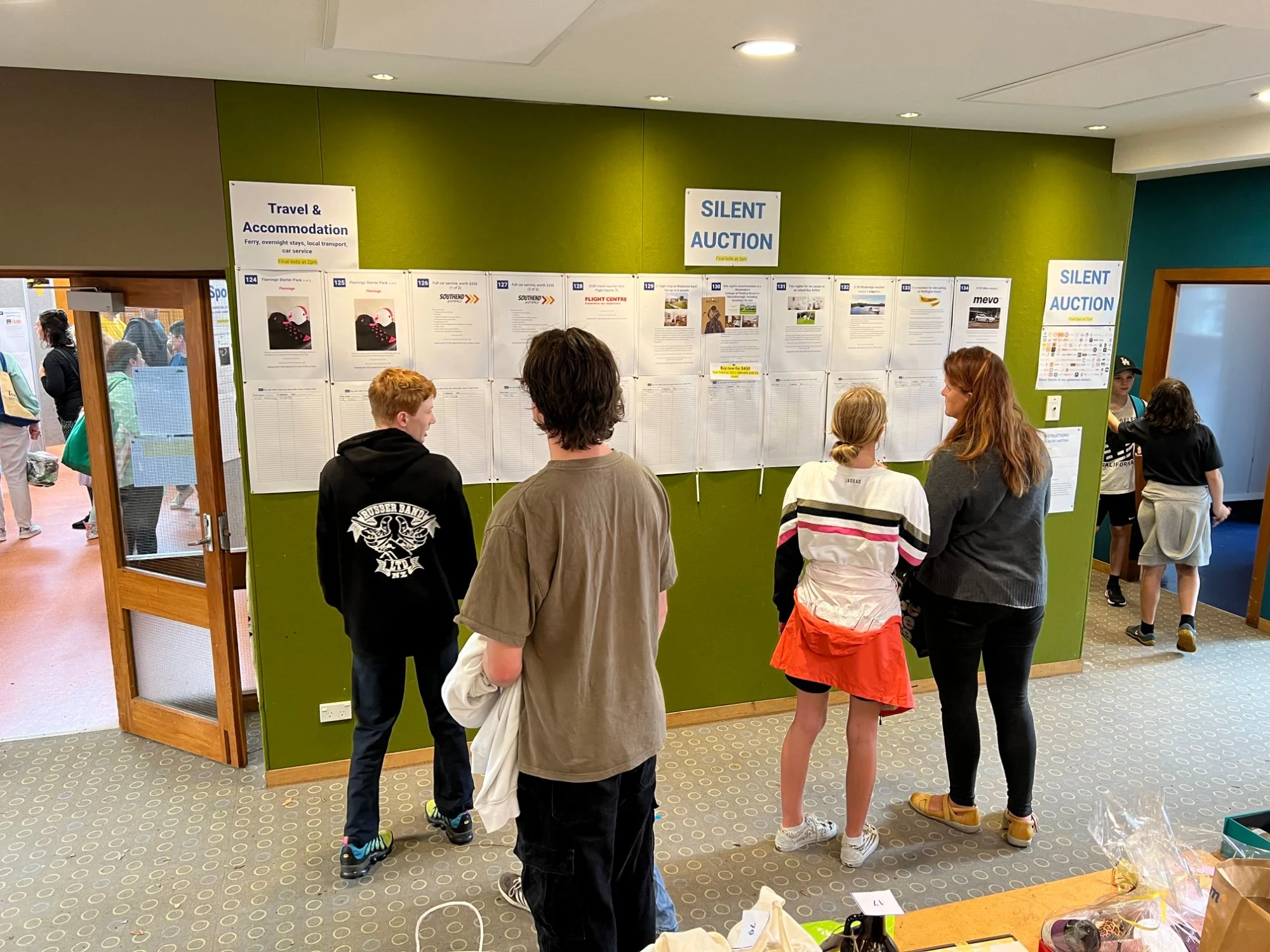 Kids and a parent reading silent auction listings on a wall at the school fair