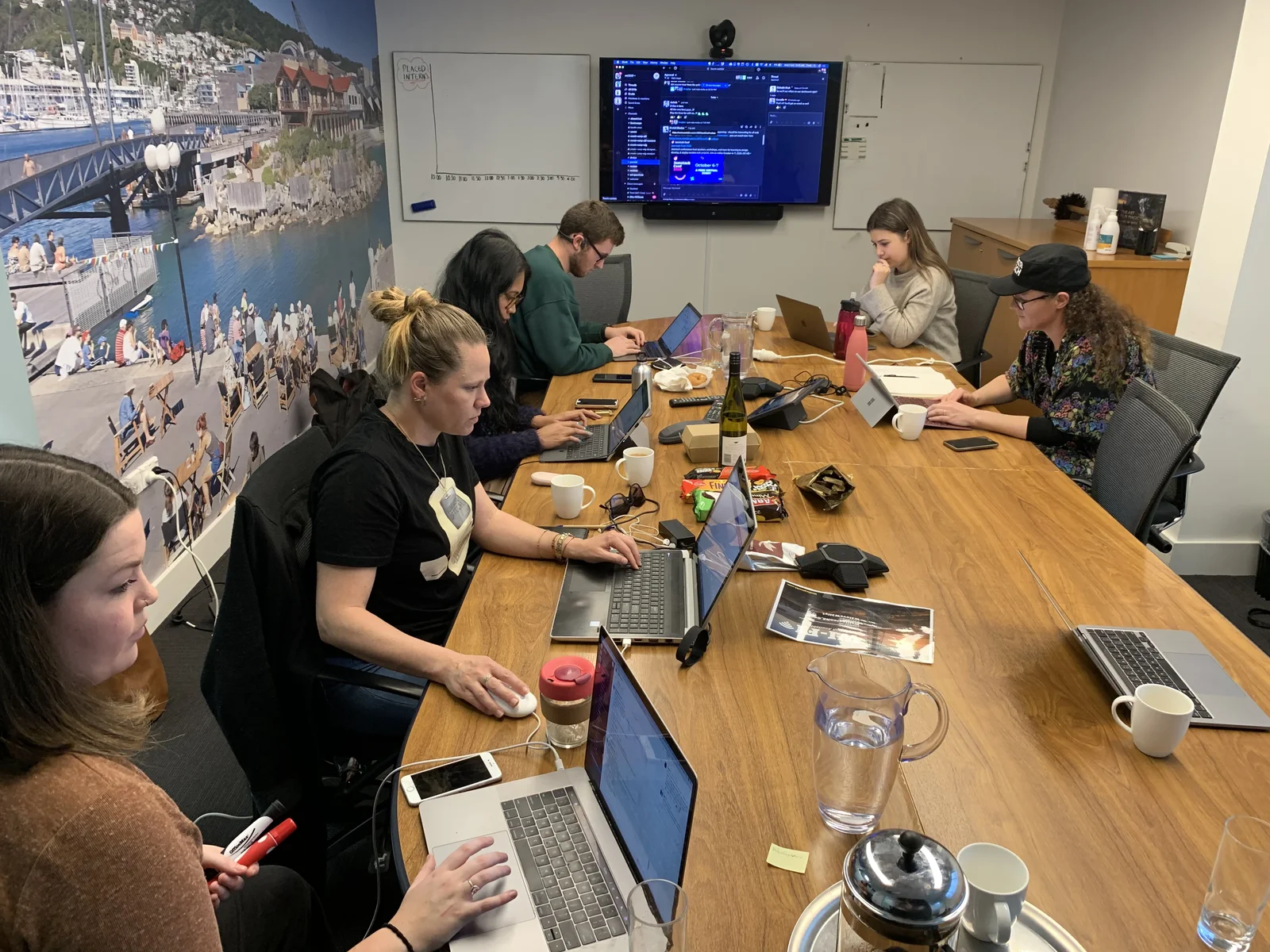 The Summer of Tech team working around a boardroom table on placement day, with a 'Placed Interns' chart on the whiteboard